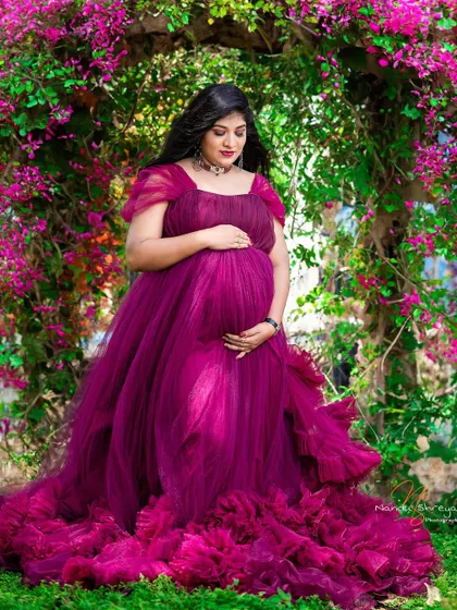 A vision in magenta, this mother-to-be stands under a floral arch, her gown blending with the vibrant flowers. This is a perfect example of a colorful garden maternity shoot.