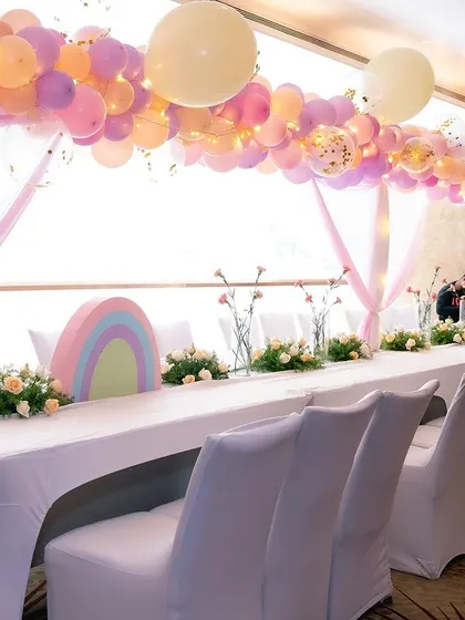The guest seating for the unicorn party featured long tables decorated with pastel rainbow cutouts, floral arrangements, and balloon arches overhead.
