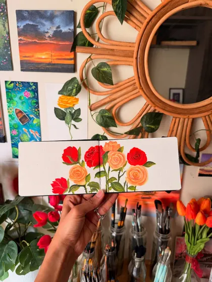The finished rose painting, held in my studio. The background shows my art wall and other fresh flowers, giving you a sense of the creative environment where your custom piece would be made.