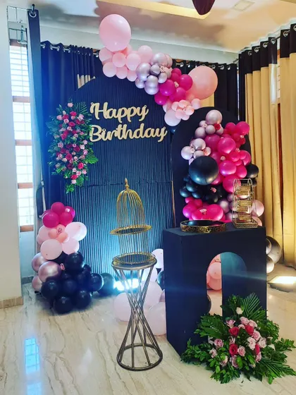 A coustamised decor for a birthday bash featuring a black arched backdrop, a pink and black balloon garland, and floral accents for a dramatic and stylish look.