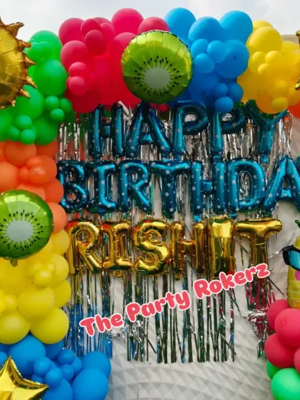 A vibrant Pool Party theme for a terrace celebration. The decor features a bright, multi-colored balloon arch, a shimmer backdrop, and fun foil balloons like a smiling sun, kiwi, and pineapple.