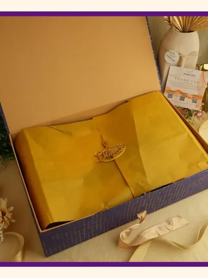 The unboxing of a royal purple hamper. The lid is removed to show the contents carefully packed with yellow tissue paper, highlighting the presentation.