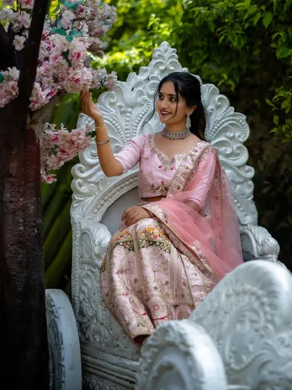 The model is seated on an ornate carriage, showcasing the fairytale quality of the pink embroidered lehenga.