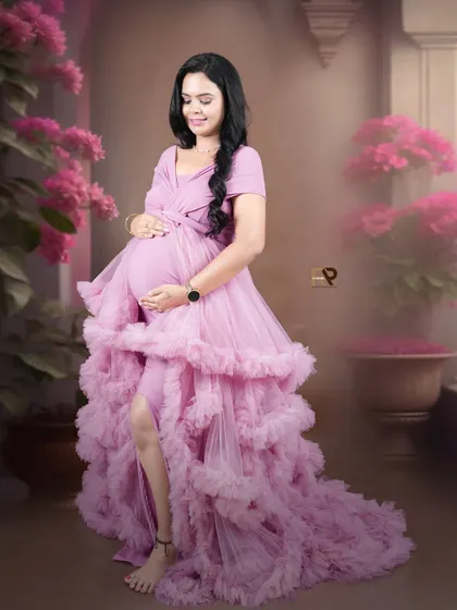 A solo portrait radiating confidence and grace. The mom-to-be stands in a beautiful ruffled pink gown against a floral backdrop, creating a soft and feminine look.