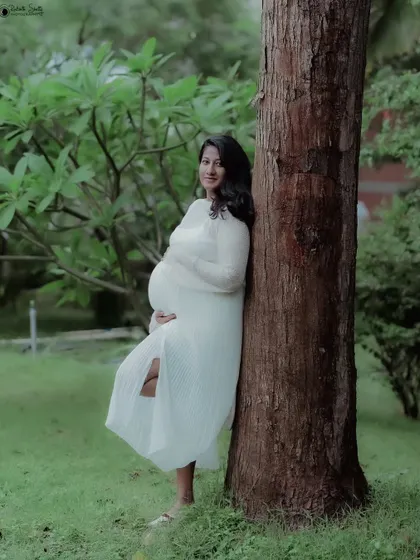 A beautiful solo shot capturing the quiet joy of pregnancy. The natural light filtering through the trees adds a soft, dreamy quality to the portrait.