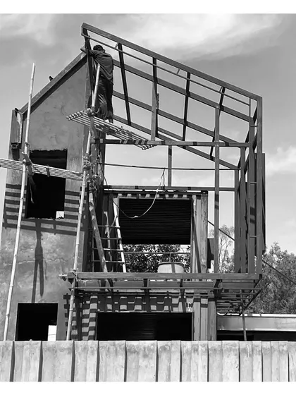A worker installs the metal roof framing on the container-based structure. This image captures the blend of prefabricated elements and on-site fabrication.