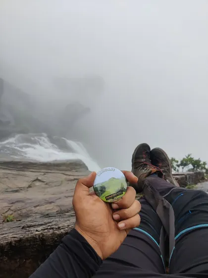 A trekker relaxes at the top of the falls, holding our Bandaje badge.