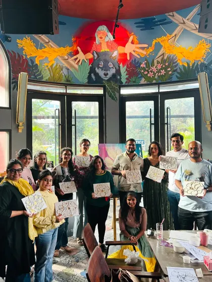 A group of beginner artists proudly holding their finished texture art pieces in a beautifully decorated cafe.