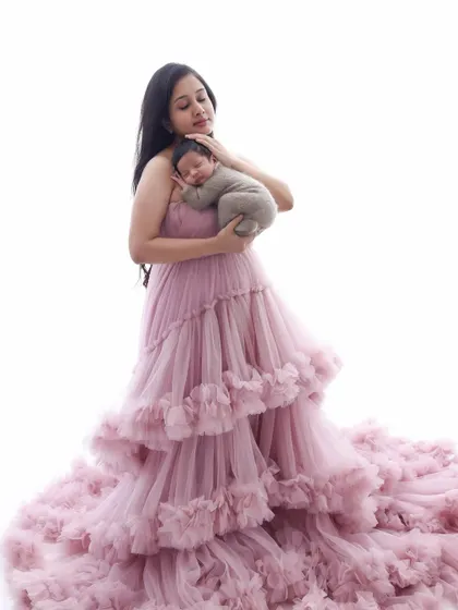 A magical portrait of a mother and her newborn. The mother's flowing pink gown creates a cloud of softness around her, cradling her tiny, sleeping baby.