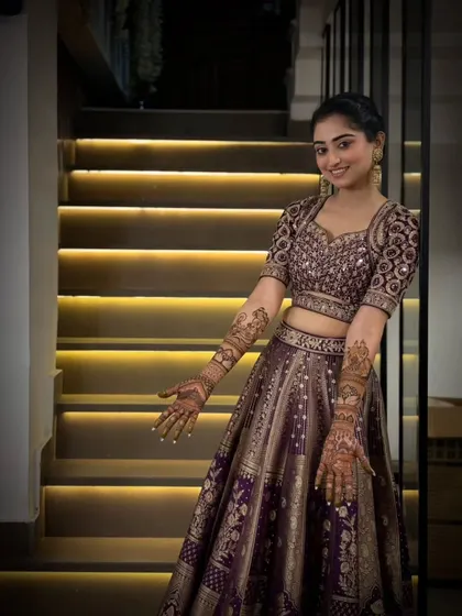 A stunning bride in a beautiful purple lehenga, showing her elegant mehandi. The design complements her outfit perfectly.