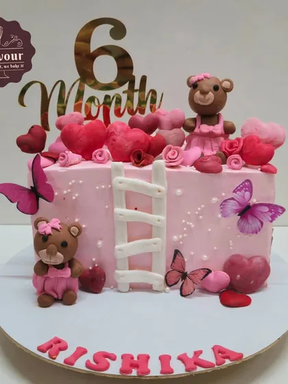 A teddy bear-themed cake for a 6-month celebration. This rectangular cake is decorated with pink frosting, hearts, butterflies, and two adorable fondant teddy bears.