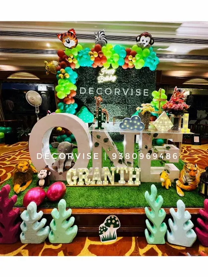 We bring the jungle to your party with our "Wild One" safari theme. This immersive setup for Granth's first birthday features a lush green backdrop, large "ONE" lettering, character cutouts of jungle animals, and themed props to create an exciting adventure for your little explorer.