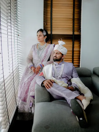 A regal and stylish portrait of a couple in lavender outfits, posing by a window.