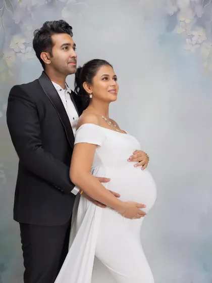 Expecting twins is a special journey. This elegant couple poses for a classic studio portrait against a painted floral backdrop, their formal attire in black and white creating a timeless look for their twin maternity announcement.