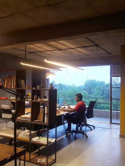 Our architecture studio in Ghitorni, designed to connect with the surrounding greenery. The open layout, custom shelving, and large glass doors create a workspace that is both inspiring and functional, with raw concrete ceilings and warm wood tones.