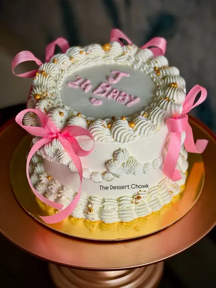 A beautiful vintage-inspired tall cake with intricate white piping and pretty pink ribbons.