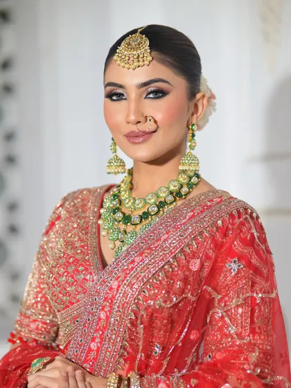 A look that turns heads and hearts. This bride is radiant in her red lehenga, with makeup that features sharp, defined eyes and a flawless base, complemented by green and gold jewellery.