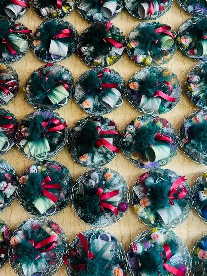 A large batch of small, round Christmas gift hampers, each wrapped in green tulle with a red ribbon. Perfect for bulk corporate giveaways.
