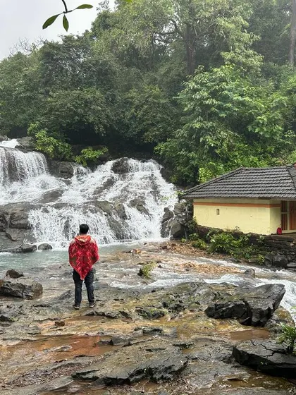 A solo trekker enjoying the view of a waterfall and temple in Uttara Kannada. A perfect moment of peace and reflection.