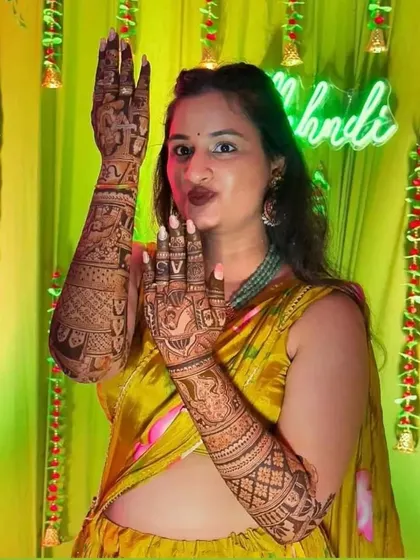 A happy bride posing and showing off her full arm mehendi at her ceremony.
