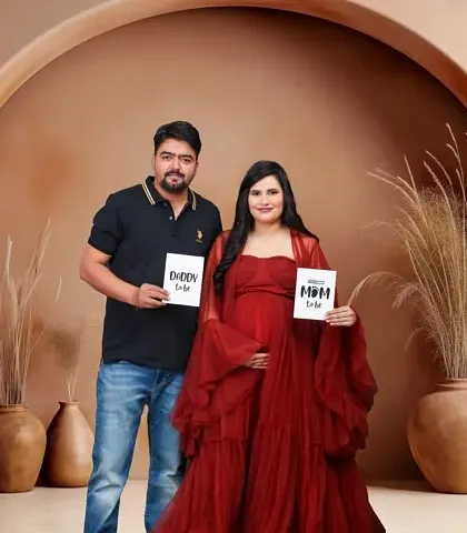 A stylish studio portrait where the couple holds "Daddy to be" and "Mom to be" signs. The earthy tones of the backdrop create a modern and warm feel for their announcement.