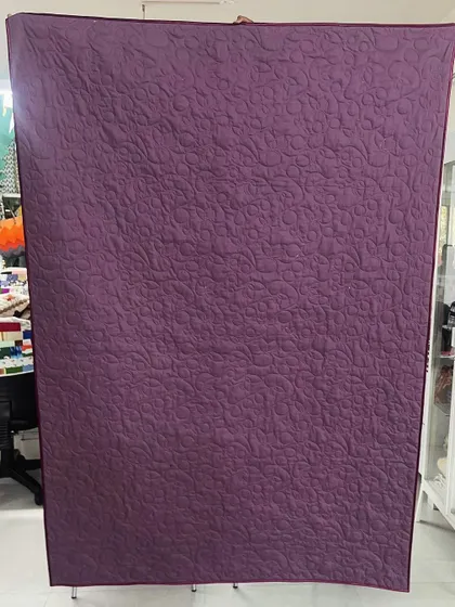 The back of a memory quilt made from a daughter's t-shirts and frocks, showing a solid purple fabric that highlights the quilting.
