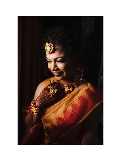 A stunning portrait of the bride during her Haldi, adorned with beautiful floral jewelry. The lighting highlights her joyful expression.