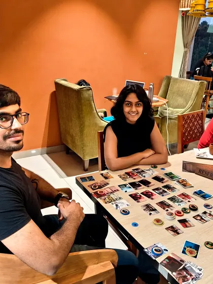 A couple enjoys a two-player game of 'Splendor'. My cafe is a great place for a casual date night filled with friendly competition.