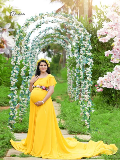 A bright and sunny portrait of a mother-to-be in a yellow gown, standing under a floral arch. The floral belt adds a lovely detail.