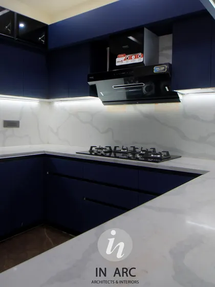 A modern kitchen design featuring handleless blue cabinets for a sleek, uninterrupted finish. The white countertop and marble-patterned backsplash provide a bright contrast.