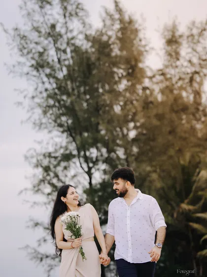 A candid moment of the couple walking hand-in-hand on the beach, sharing a laugh. It's a simple, happy memory from their pre-wedding shoot.