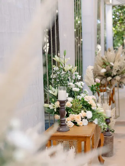 A close-up of a floral arrangement on a wooden console table, part of a chic and airy boho-themed Roka ceremony.