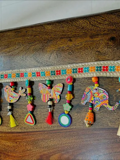The 'Bageecha' Toran laid out on my wooden table. It’s made with wooden birds, elephants, and butterflies featuring my art prints, plus bells, beads, and tassels. This one is sold, but I can always make a unique piece just for you.