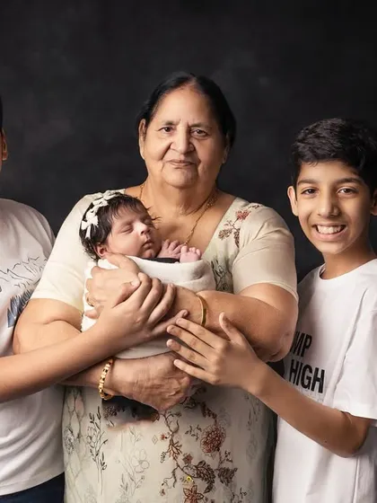 A grandmother's warm embrace for her newborn grandchild, with two proud older brothers looking on. This is a beautiful portrait of sibling and intergenerational love.