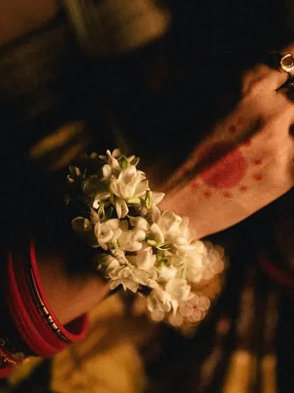 A close-up detail of the bride's hands, adorned with alta and floral bracelets. This shot focuses on the beauty and symbolism of traditional bridal adornments.