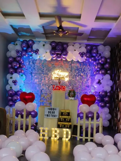This birthday decoration uses a beautiful purple and white color palette. The floor is covered in light-colored balloons, making the space feel bright and airy.