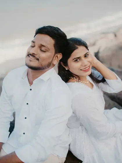 A relaxed and happy portrait of a couple sitting back-to-back on beach rocks.