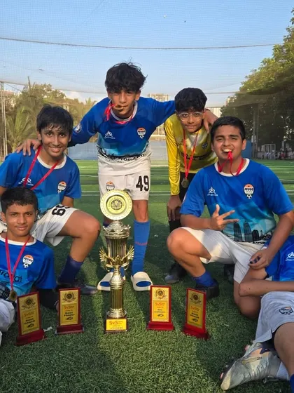 The U-15 champions relaxing on the pitch with their medals and trophies after a hard-fought tournament.