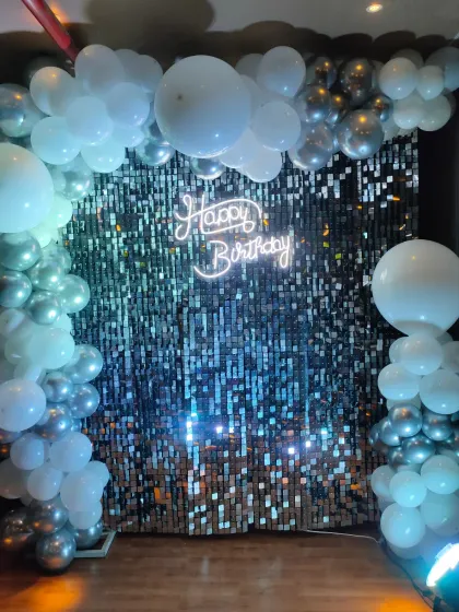 A clean and elegant look with a silver shimmer wall, framed by a simple arrangement of white and silver-grey balloons.