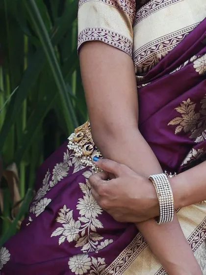 This shot focuses on the detail of the purple silk dupatta with its gold floral patterns, draped over the arm.