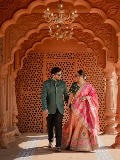 The couple walks hand-in-hand through a grand, architecturally rich corridor during their pre-wedding photoshoot, creating a royal and timeless image.