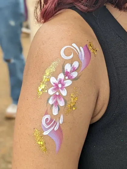 A floral arm tattoo with pink flowers and a swirl of gold glitter.