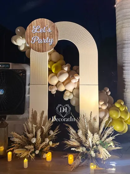 A modern and stylish "Let's Party" photo point. This setup features a ribbed arch backdrop, a neutral-toned balloon garland, and arrangements of dried wheat and pampas grass, perfect for a contemporary boho theme.