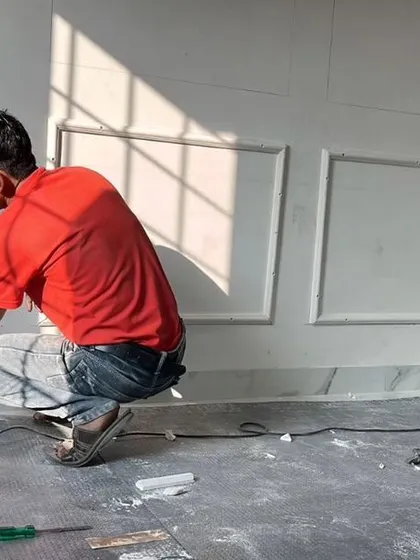 Our skilled craftsmen are seen here meticulously installing the base molding on a paneled wall. This image offers a glimpse into the precision and hands-on work that goes into achieving a flawless finish.