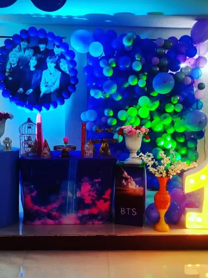 For older kids and teens, I can create themes based on their favorite bands, like this BTS-themed party. The setup uses dramatic blue and purple lighting, a custom photo backdrop, and a light-up number.