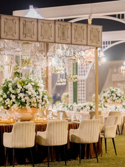 An elegant outdoor cocktail reception setup, with hanging crystal chandeliers, plush seating, and beautiful floral arrangements.