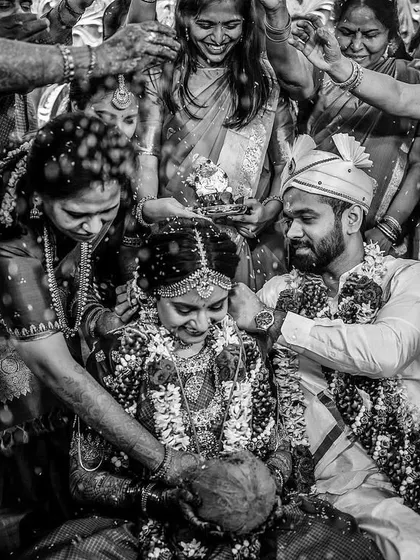 A dramatic black and white photo of a couple being blessed by their families. The high contrast emphasizes the emotion and the flurry of activity, creating a powerful image of this important ritual.