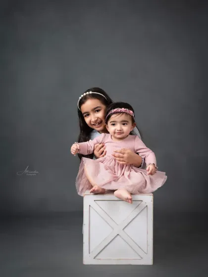 A playful moment between sisters, with the older one giving her baby sister a loving hug.