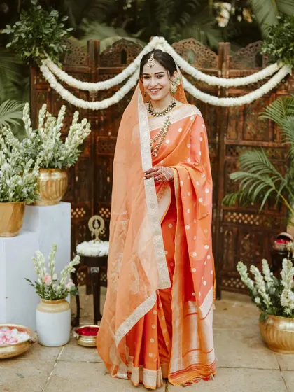 A full-length shot of the bride in her beautiful orange saree. The minimal glam makeup complements the vibrant color of her outfit perfectly.