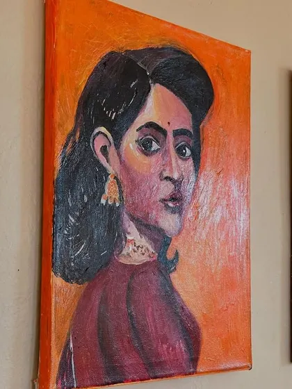 A close-up of one of my acrylic on canvas portraits. This piece features a woman with an introspective gaze, set against a warm orange background that highlights her features.